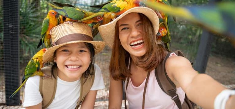 a parent and child in hats smile for pictures while surrounded by birds